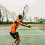 man in orange shirt and black shorts holding black and white tennis racket