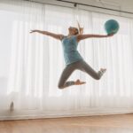 Slim woman in sportswear jumping up with ball