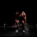 topless man in black shorts sitting on black and silver barbell