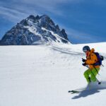 man in orange jacket and black pants riding ski blades on snow covered mountain during daytime