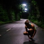 a woman squatting down on a road at night